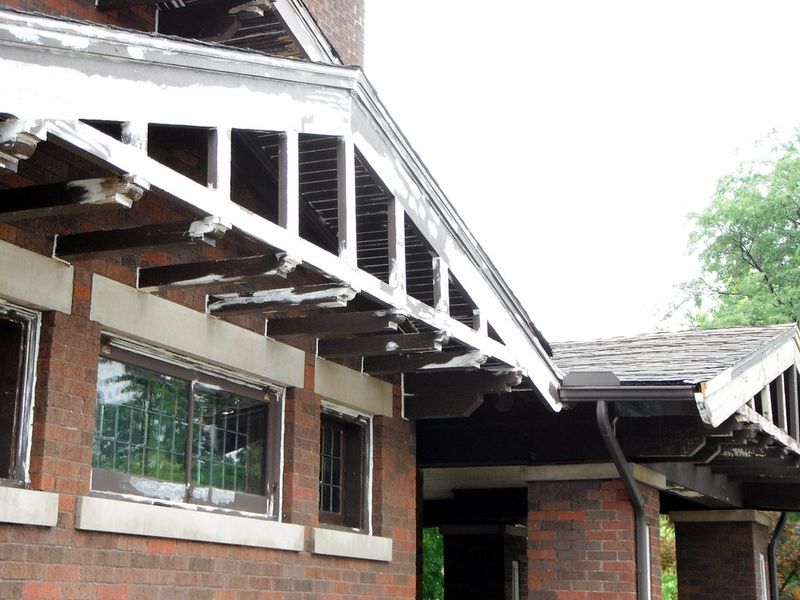 A brick bungalow with exposed rafter tails and peeling paint along its eaves