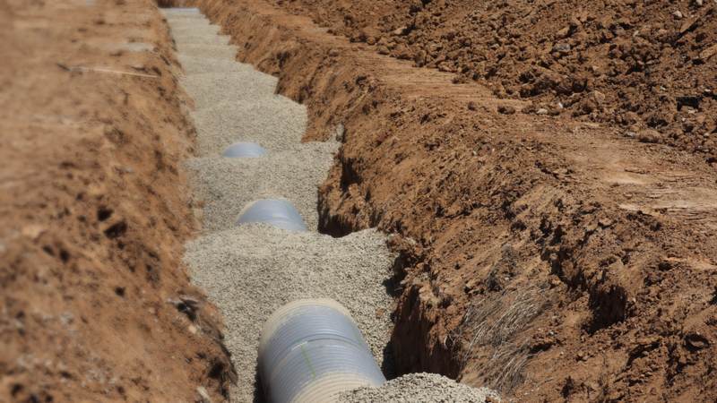 A drainage trench with pipe bedded in gravel, cut through bare earth