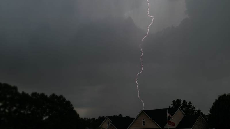 A lightning bolt over the rooflines of houses under a dark storm sky