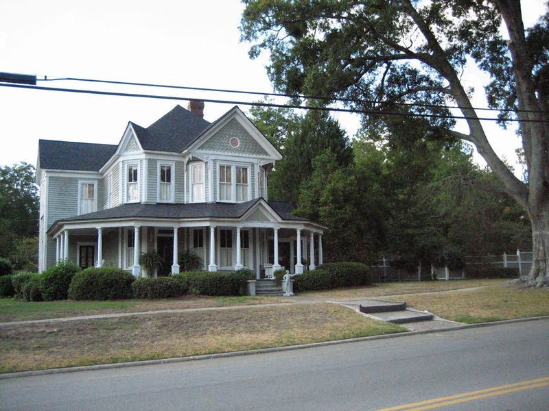 A two-story Victorian house with a wraparound columned porch beside a large oak in McRae-Helena, the Telfair County seat next to Wheeler County