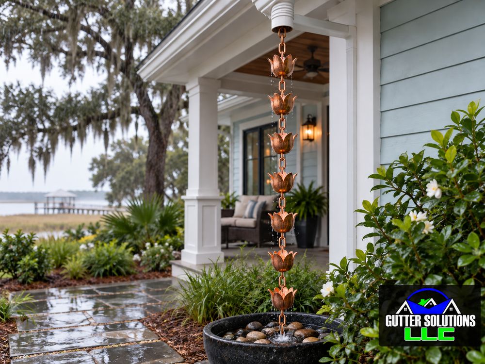Copper cup rain chain with visible metal links carrying rainwater into a pebble-filled basin.